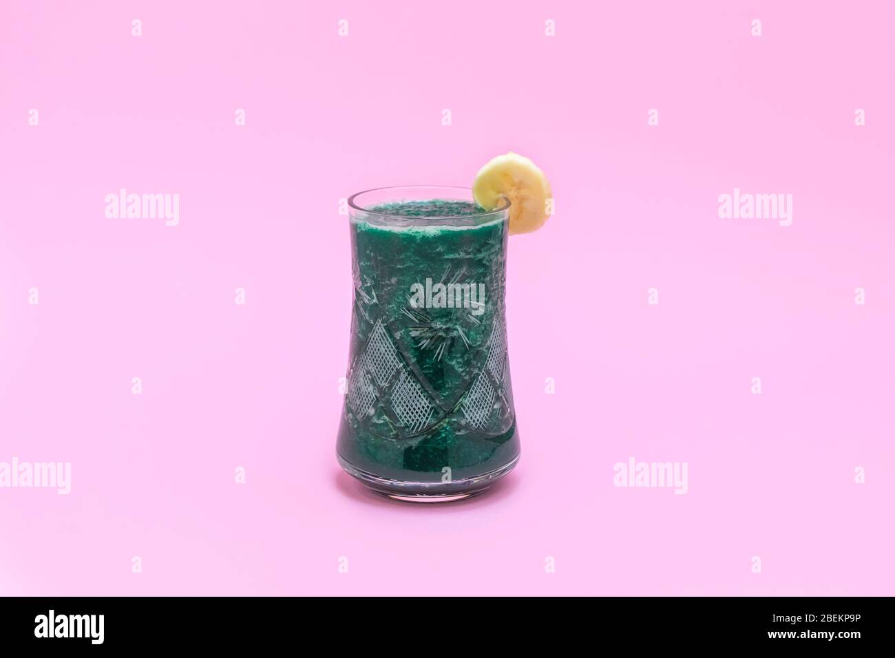 Tazza di frullato verde con banana su sfondo rosa pastello con spazio per il testo Foto Stock