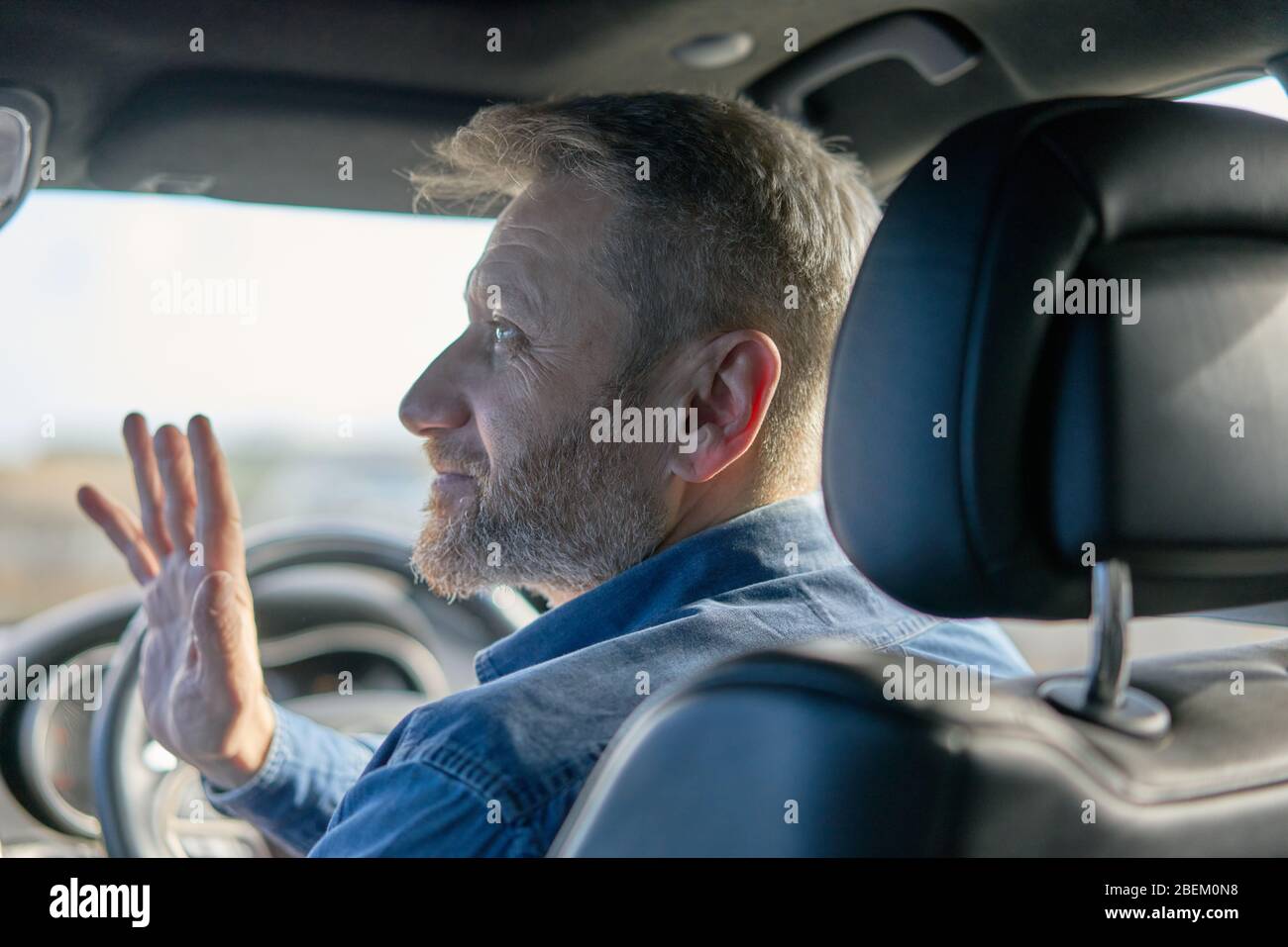 Profilo di un simpatico autista con capelli e barba ghiaiosi presi dall'interno dell'auto Foto Stock