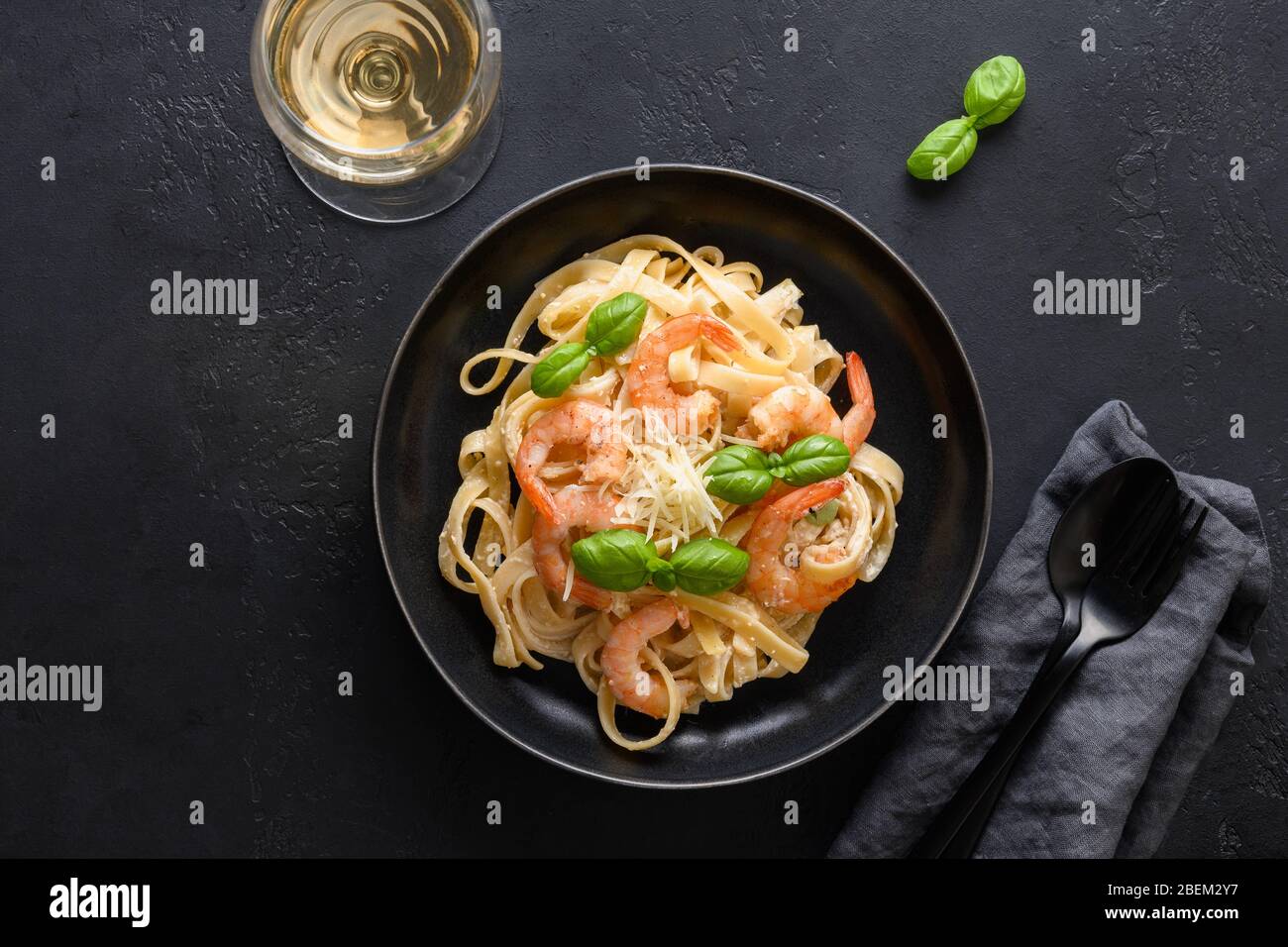 Fettuccine di pasta italiana con gamberi e bicchiere di vino bianco su tavola nera. Foto Stock