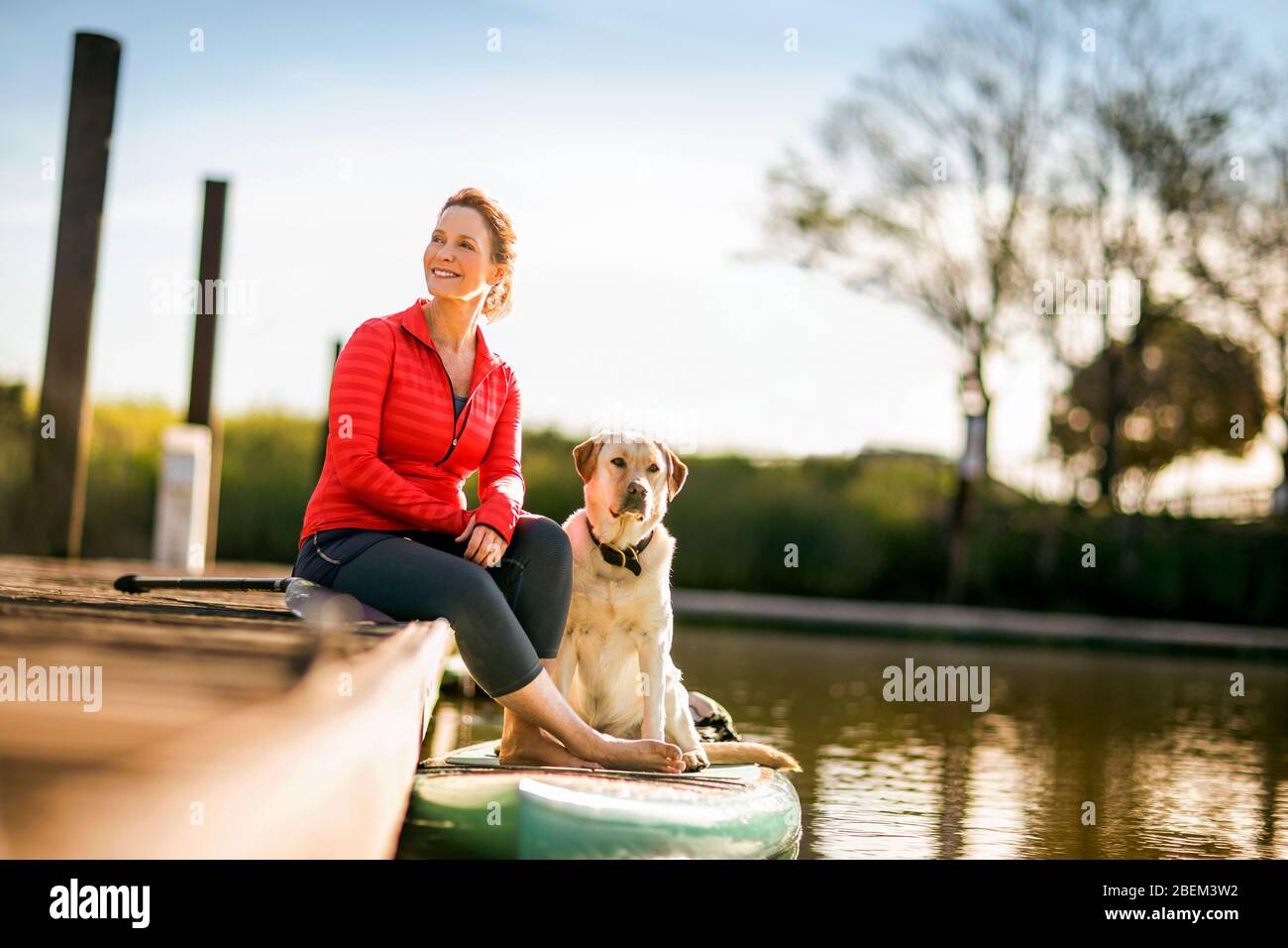 Donna di mezza età adulta seduta su un molo con il suo cane Foto Stock