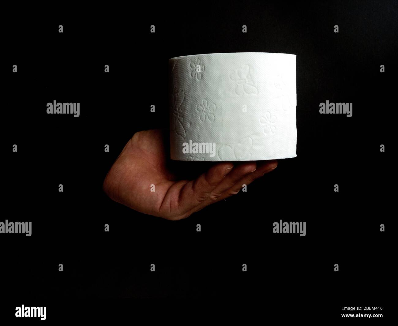 Mano di un uomo tiene un rotolo di carta igienica bianca isolato su sfondo nero Foto Stock