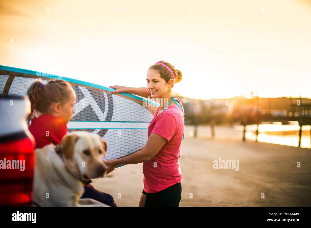 Madre e figlia che si preparano ad andare a paddle board con il loro cane Foto Stock