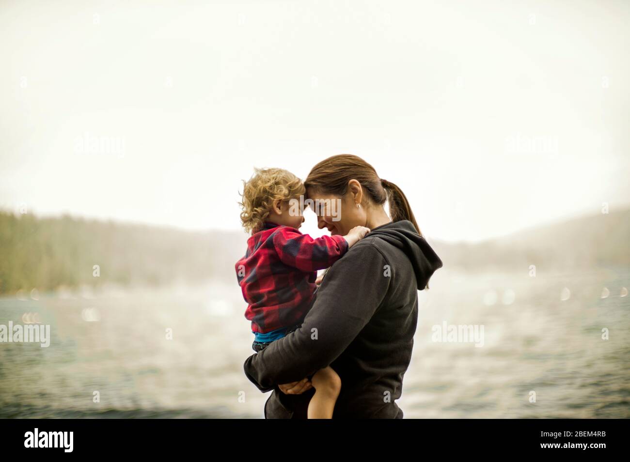Madre di mezza età che tiene il suo figlio giovane sulla riva di un lago Foto Stock