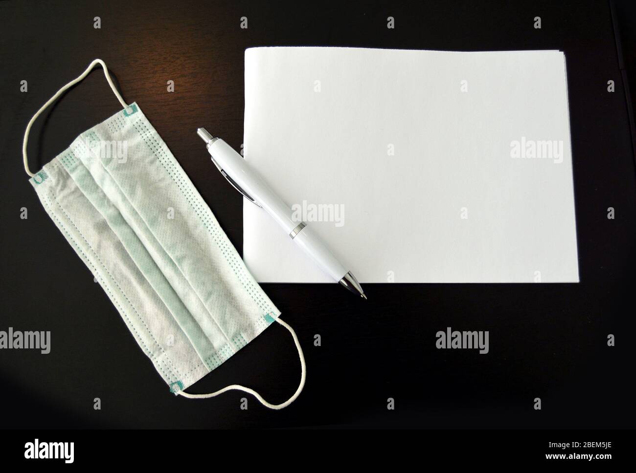 Primo piano di blocco note, penna e maschera, facemask sulla scrivania accanto a carta blocco note e penna grande per il titolo Foto Stock