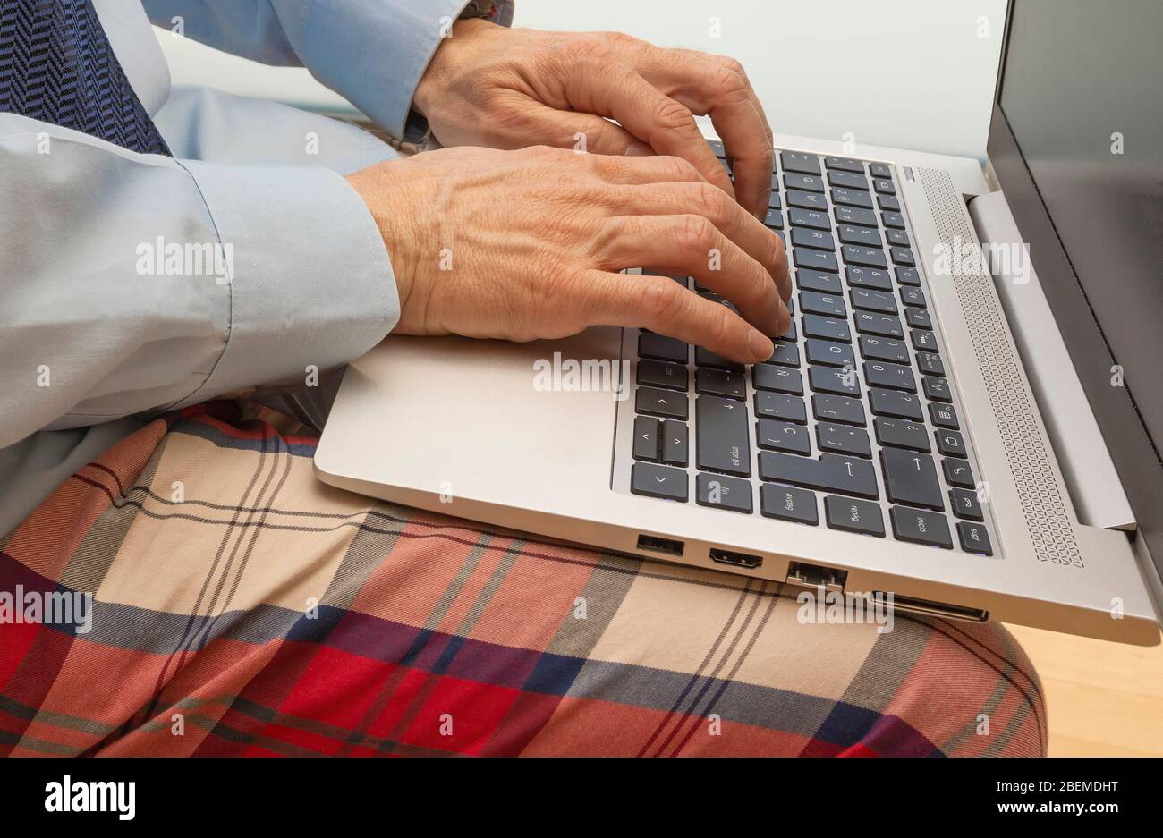 Dettaglio delle mani di un uomo che utilizza la tastiera di un portatile e un abito con una camicia, cravatta e pigiama concetto di telelavoro Foto Stock