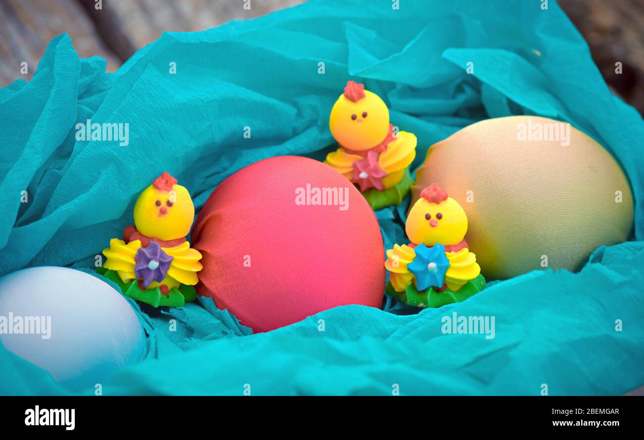 Tre pollo dolce e tre uova di pasqua colorate su un panno blu in un cestino Foto Stock