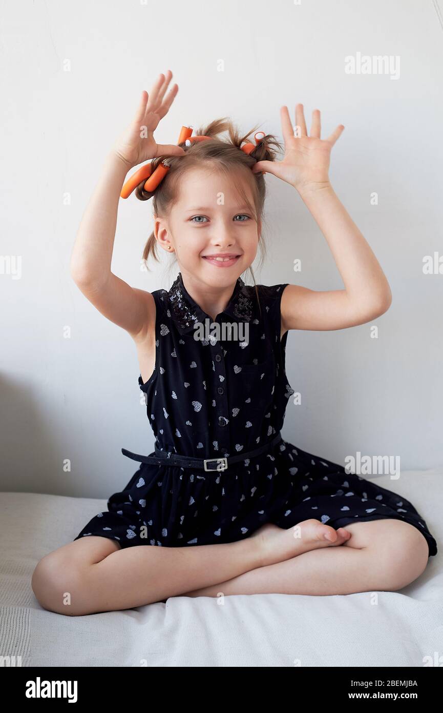 Una bambina di 6 anni con arricciacapelli sulla testa, che si aggira intorno. La ricerca delle gioie di beauty.Children. Isolato su sfondo bianco. Foto Stock