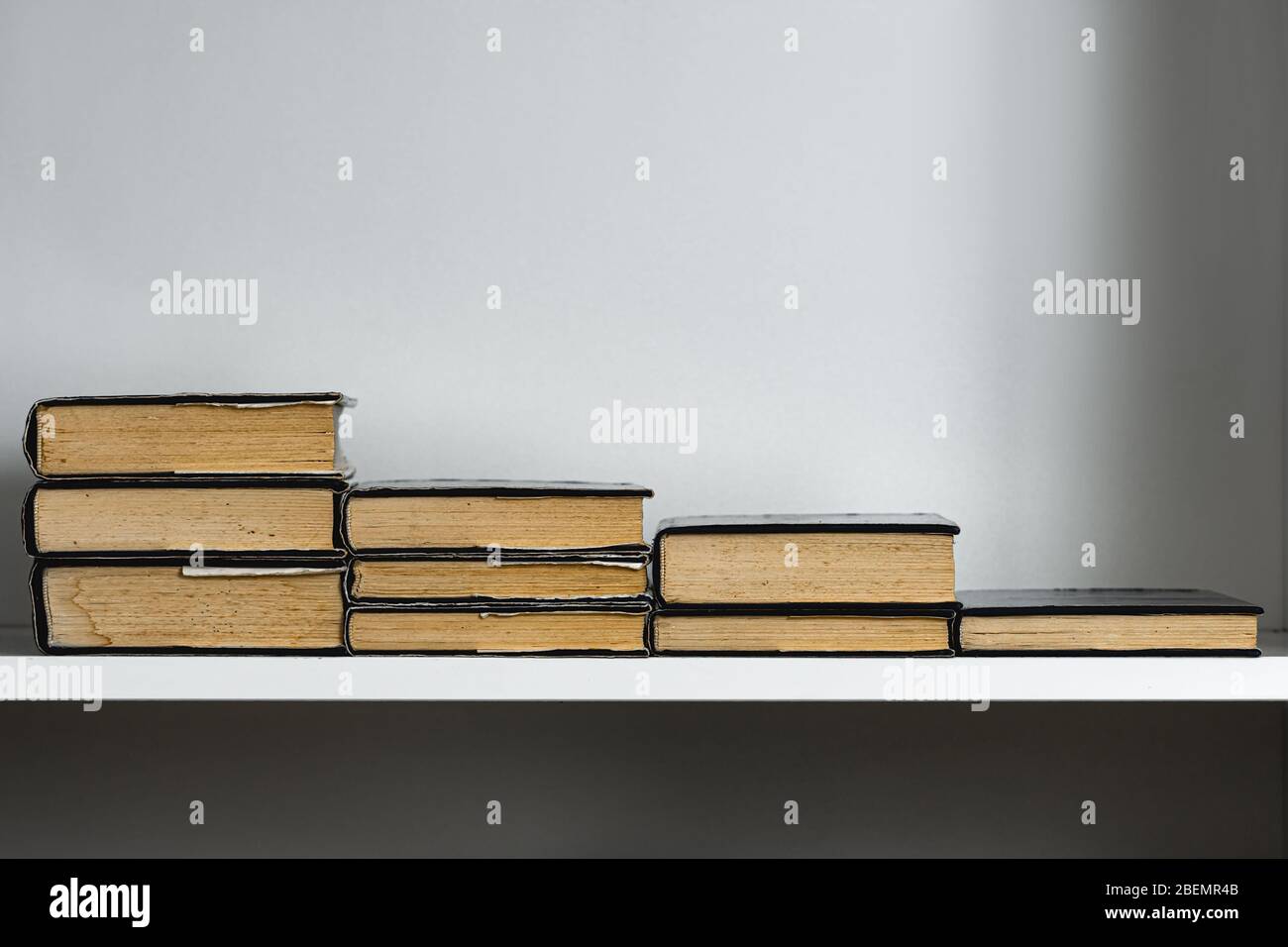 Vecchi libri sulla mensola bianca allineati come scale con copy space concetto Foto Stock