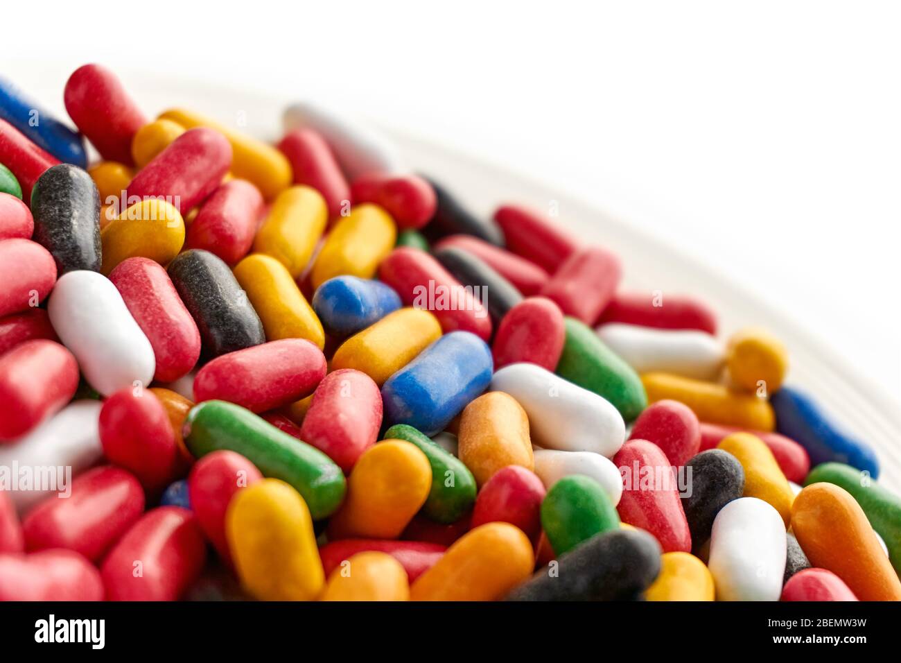 Primo piano di caramelle dolci colorate e lucide in blu, rosso, giallo, verde, nero e bianche su piattino. Angolo olandese con spazio di copia. Foto Stock