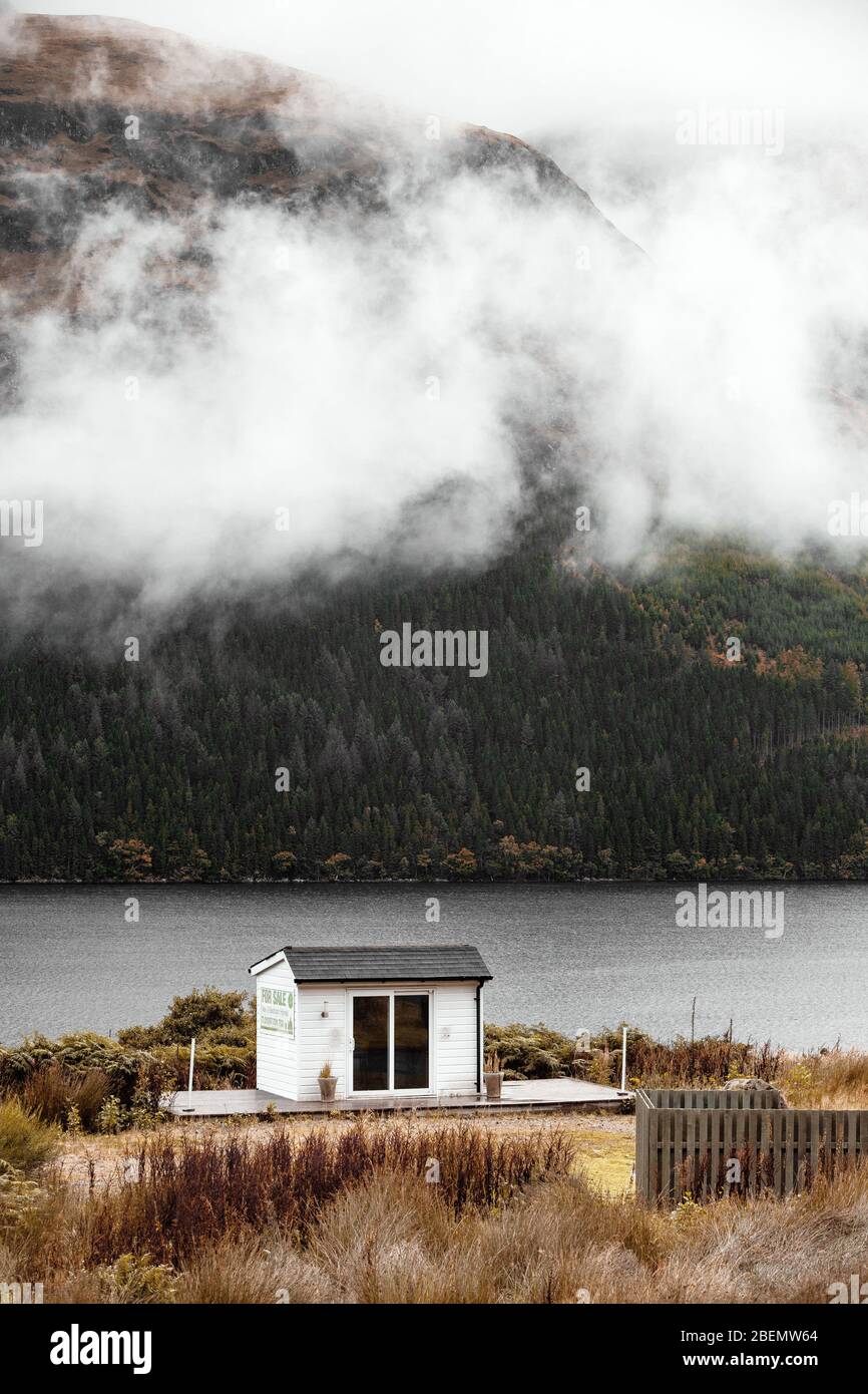 Singola Casa isolata nel mezzo delle montagne con nebbia che si avvolge attraverso il lago Foto Stock