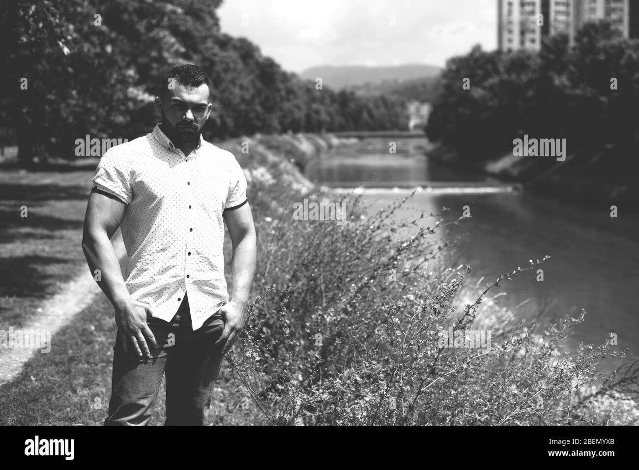 Ritratto di un giovane uomo sicuro e di successo con T-shirt bianca in piedi all'esterno in Park Foto Stock