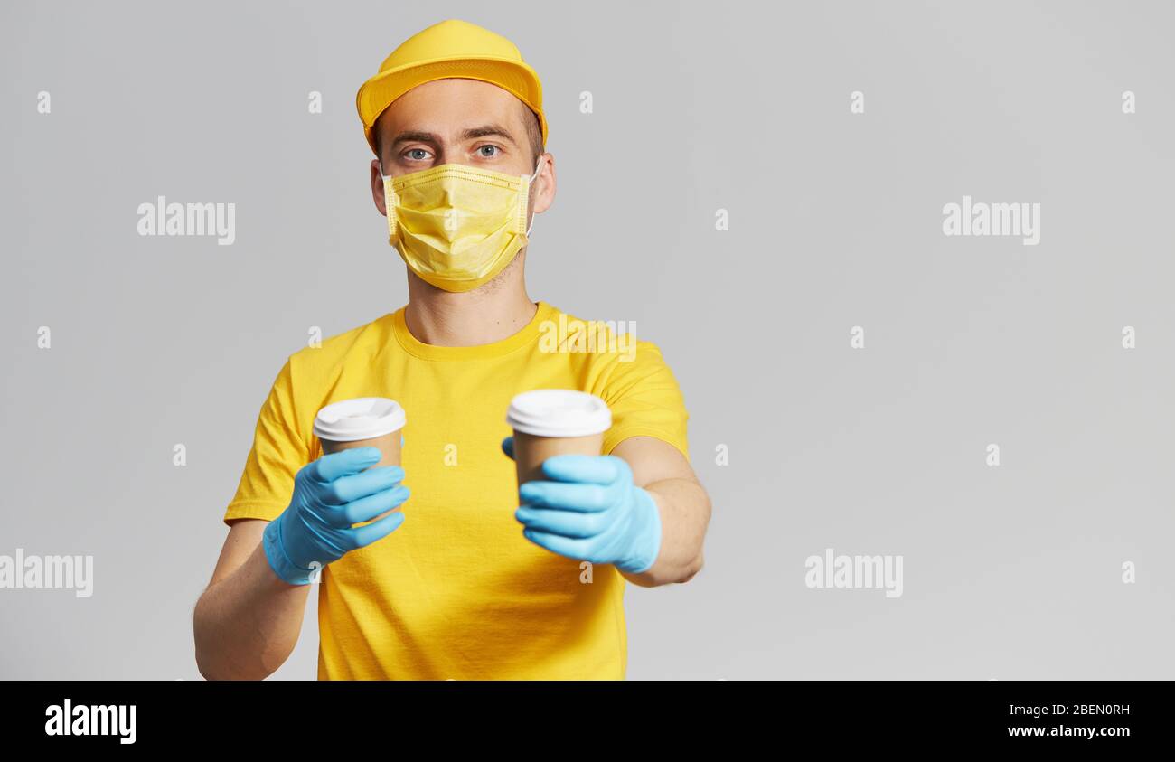 Pacchetto alla porta. Corriere in uniforme gialla, maschera protettiva e guanti per la consegna del caffè da asporto. Servizio di consegna in quarantena. Spazio per il testo Foto Stock