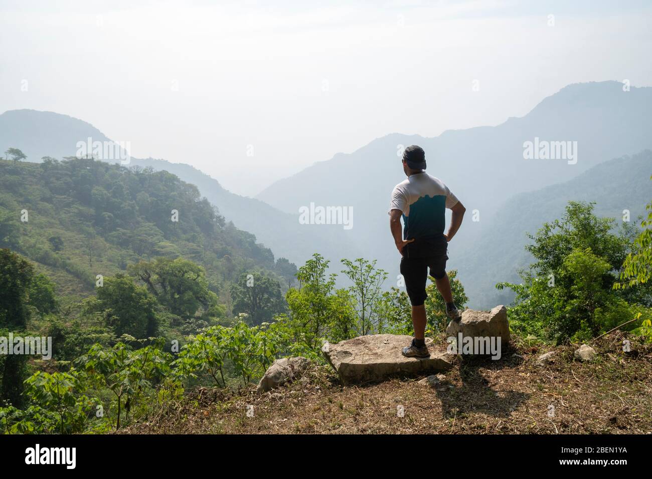 Un uomo si trova su una roccia che guarda il paesaggio montano Foto Stock