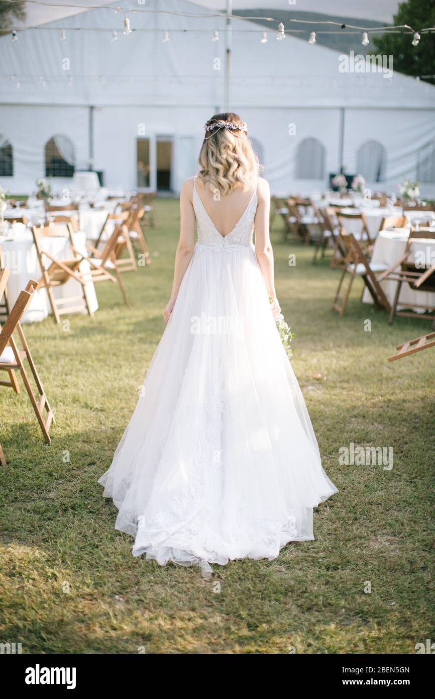 La sposa si pone mostrando la schiena. Mentre il sole tramonta, al luogo del matrimonio. La sposa tiene in mano un fiore nuziale. / Camicie della sposa. Foto Stock