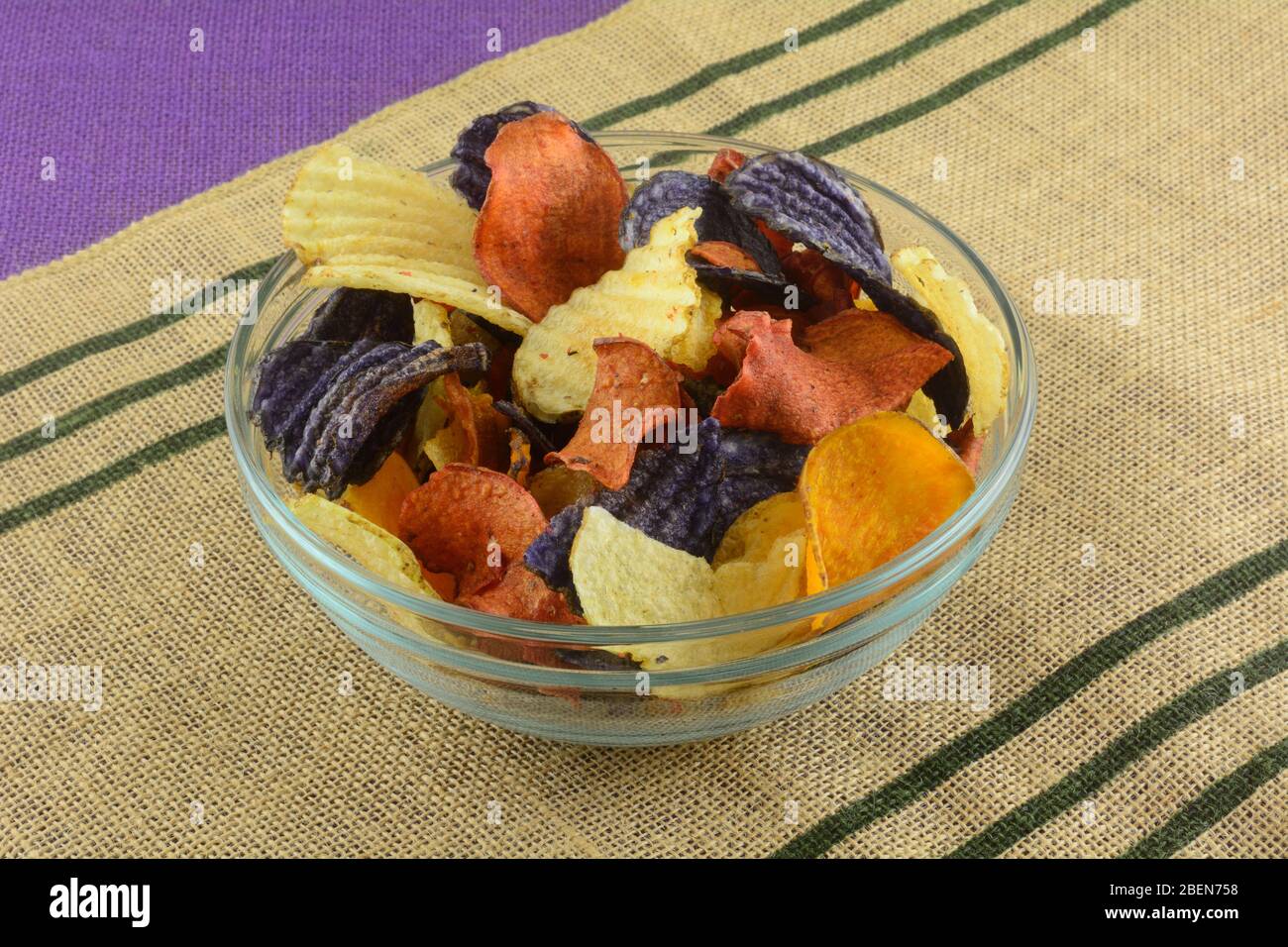 Patatine vegetali a base di patate d'oro yukon, patate blu e patate dolci in una ciotola di vetro per snack sul tappetino Foto Stock