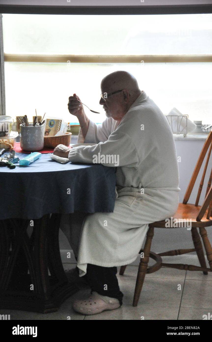 Un uomo più anziano siede da solo a mangiare la colazione Foto Stock