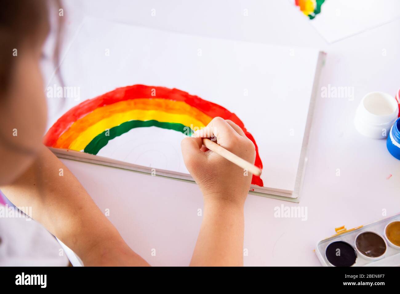 Soggiorno a casa a causa del concetto pandemico coronavirus. La bambina dipinge un arcobaleno sul poster di soggiorno a casa. Insegui il flashmob arcobaleno. Attività positive Foto Stock