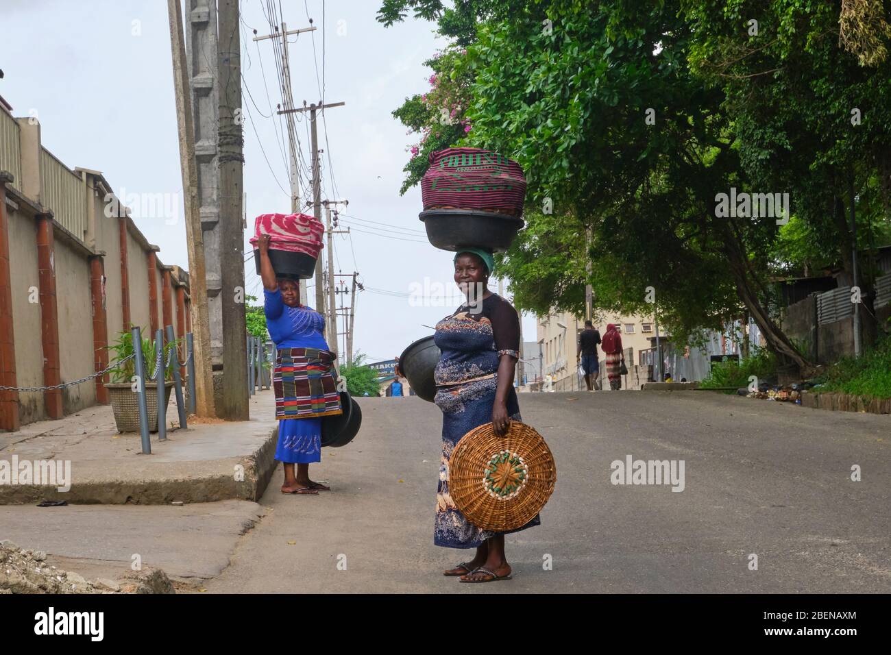 Due donne si fermano a posare per una foto mentre camminano verso il mercato con i loro beni sulla testa a Lagos, Nigeria. Foto Stock