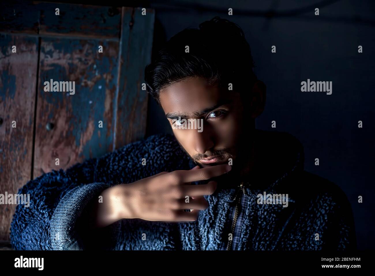 Ritratto di giovane barba maschile modello indossando un maglione di lana blu scuro e posando girato con tecnica di luce Rembrandt sul suo viso in nero Foto Stock