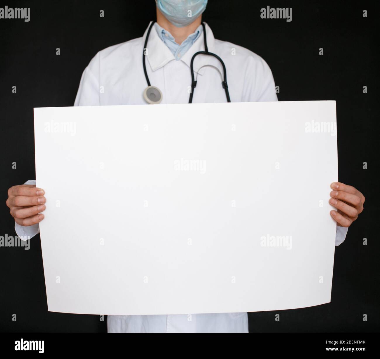 Un uomo in una t-shirt nera e guanti medici tiene un foglio bianco di carta. Mockup. Coronavirus. Quarantena . Epidemia. Spazio di copia. Avvertenza. Mano del medico in guanto blu che tiene fogli di carta. Foto Stock