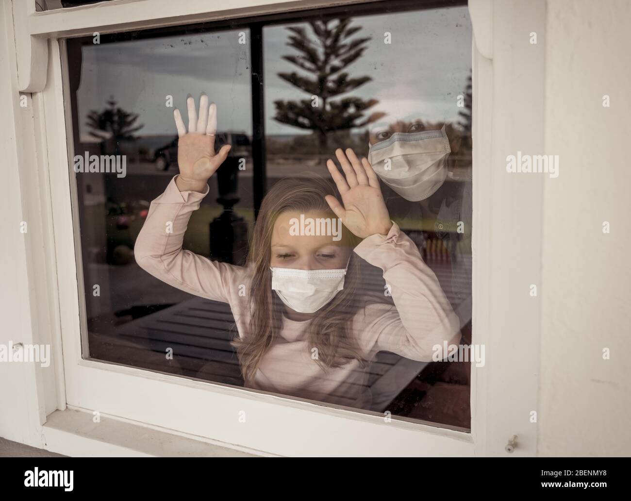Blocco COVID-19. Bambina solitaria depressa con maschera facciale che guarda attraverso la finestra durante la quarantena. Triste bambino malato in isolamento di auto a casa. Foto Stock