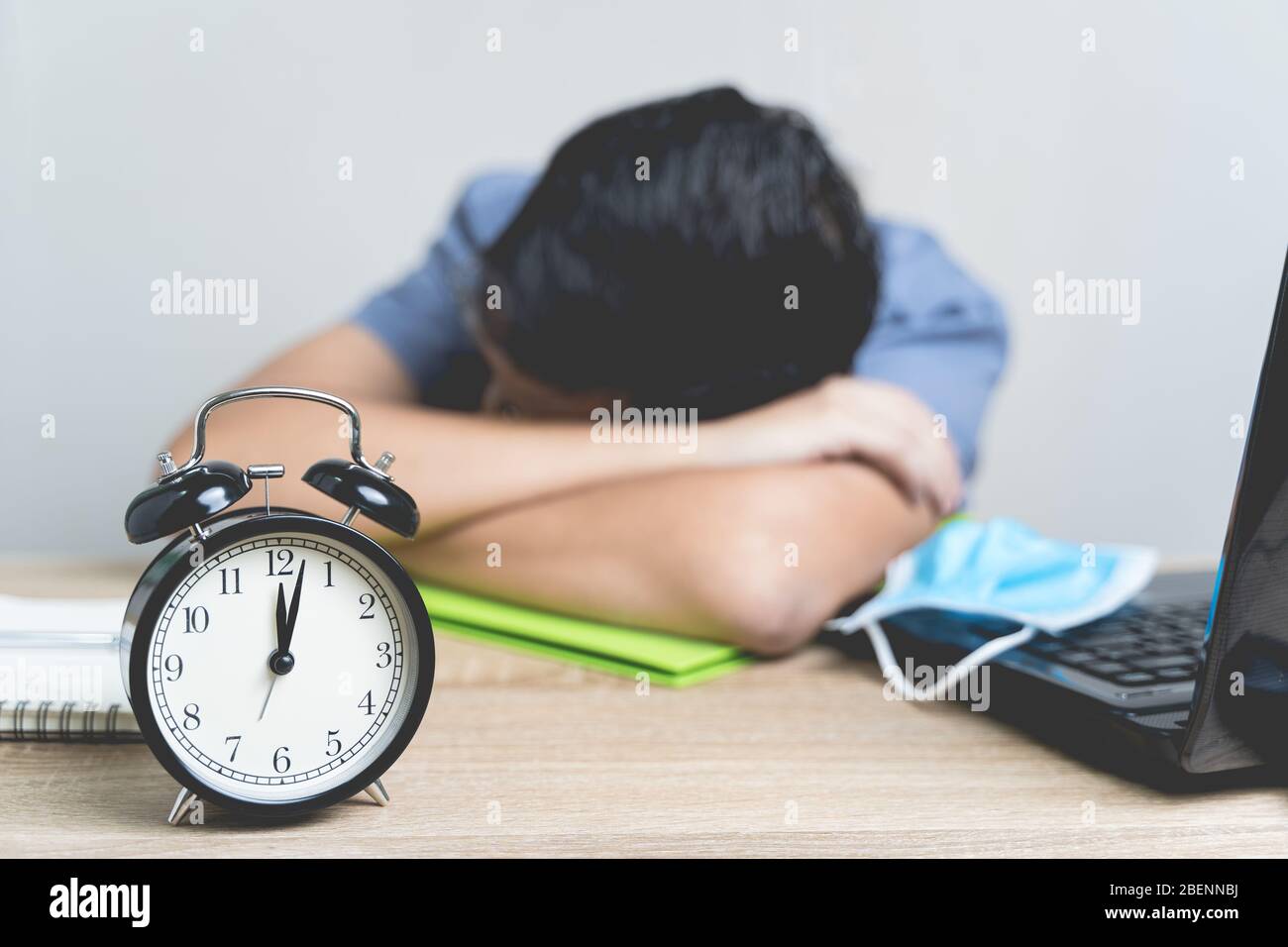 Lavoro da casa durante lo scoppio del virus. Sveglia sveglia sul tavolo a mezzanotte con sfocatura l'uomo d'affari lavora da casa e lui è bec dormire Foto Stock