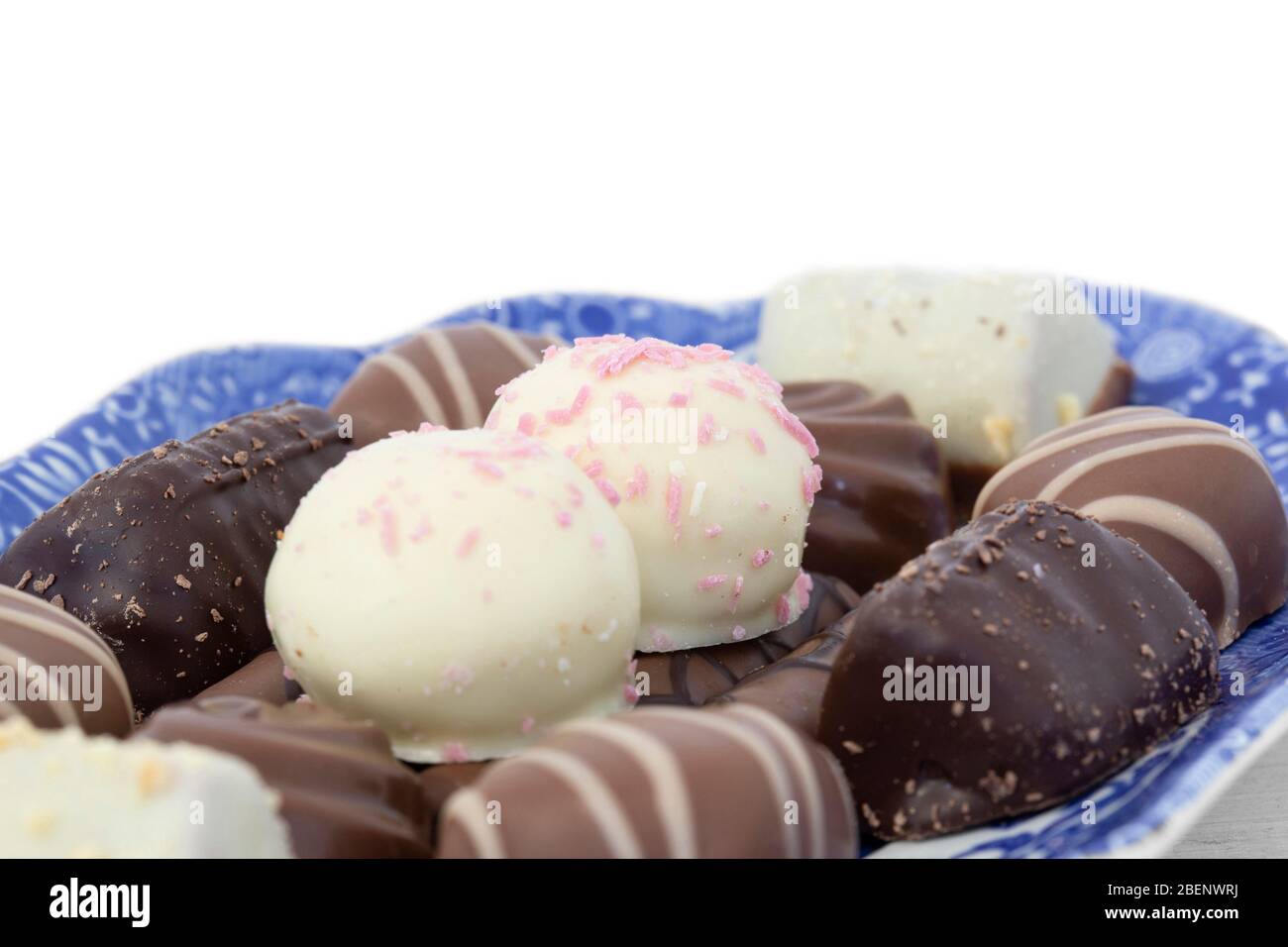 Selezione di cioccolatini su un piatto con motivi blu e bianchi. Su sfondo di legno bianco Foto Stock