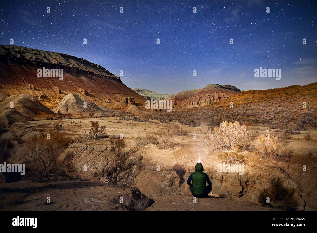 Uomo con luce di testa seduto per terra nel deserto di notte sullo sfondo del cielo. Viaggi, avventuri e concetto di spedizione. Foto Stock