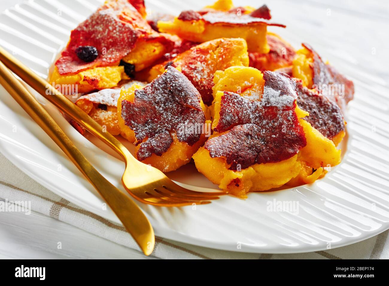 Cucina austriaca: Pancake sminuzzati kaiserschmarrn con uvetta e zucchero a velo servito su un piatto bianco con posate dorate su uno sfondo di legno Foto Stock