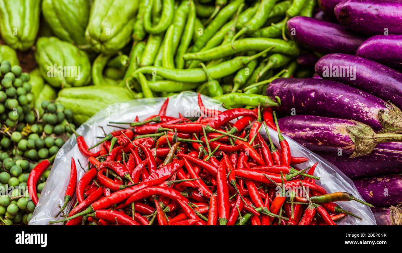 Primo piano di peperoncino fresco e rosso e di altre verdure esotiche in vendita su un mercato asiatico di strada Foto Stock