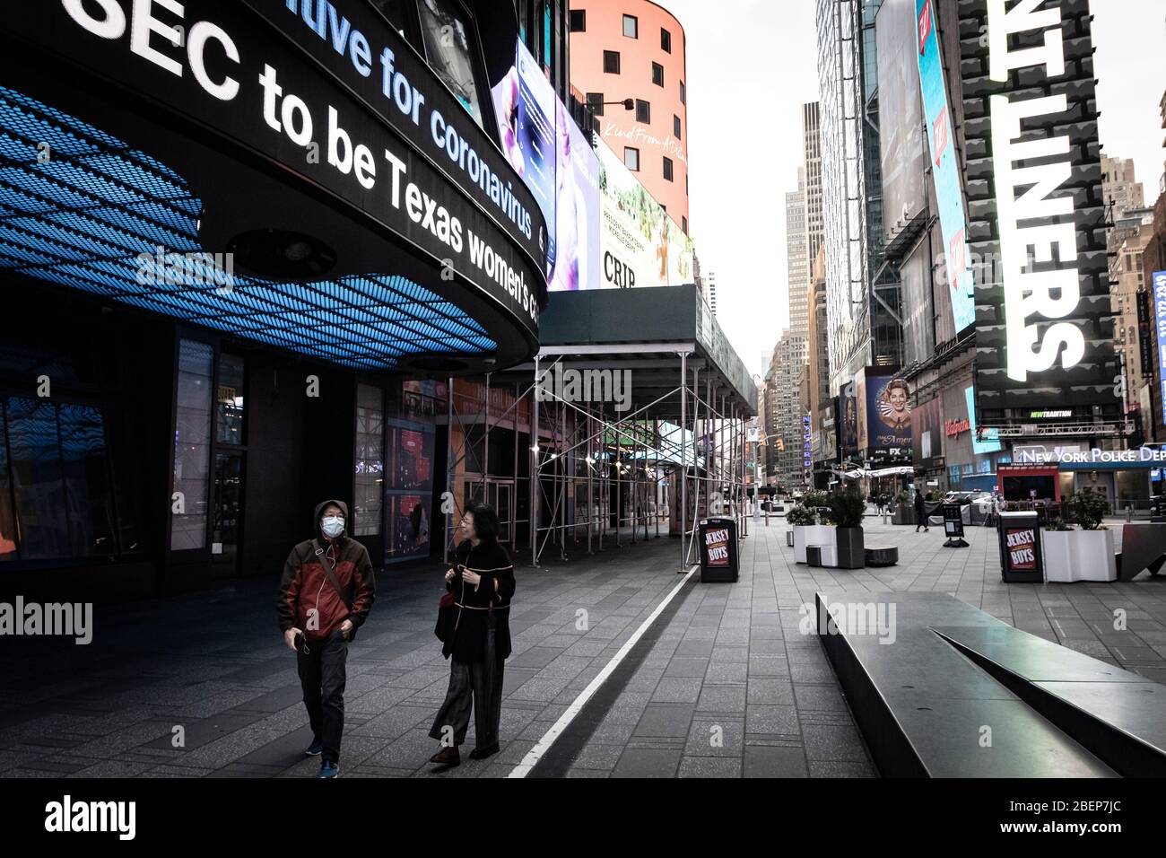 Due persone camminano da sole in zona vuota di Times Square; titolo di coronavirus sopra in notiziario. Foto Stock