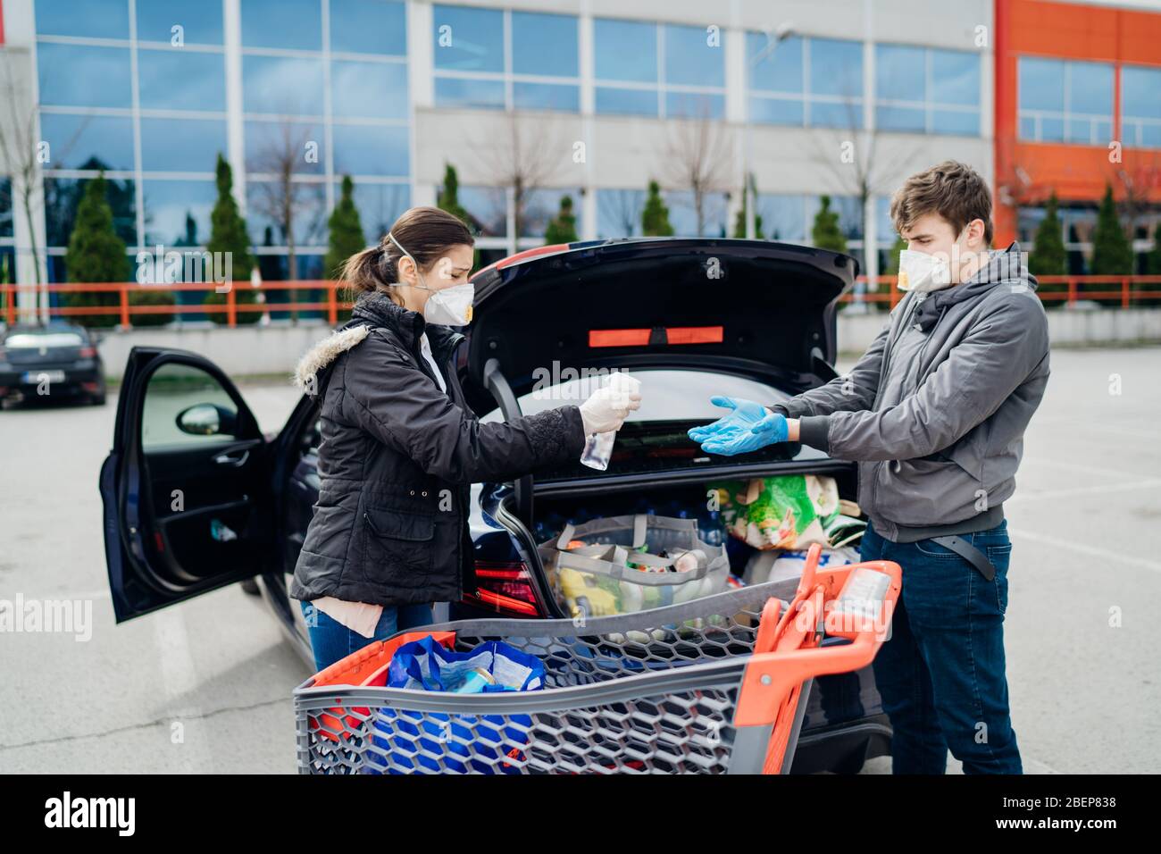 Coppia spaventata che indossa maschere e guanti disinfettanti prodotti dopo lo shopping per alimentari / forniture in supermarket.Using spray disinfettante.Coronavirus Foto Stock