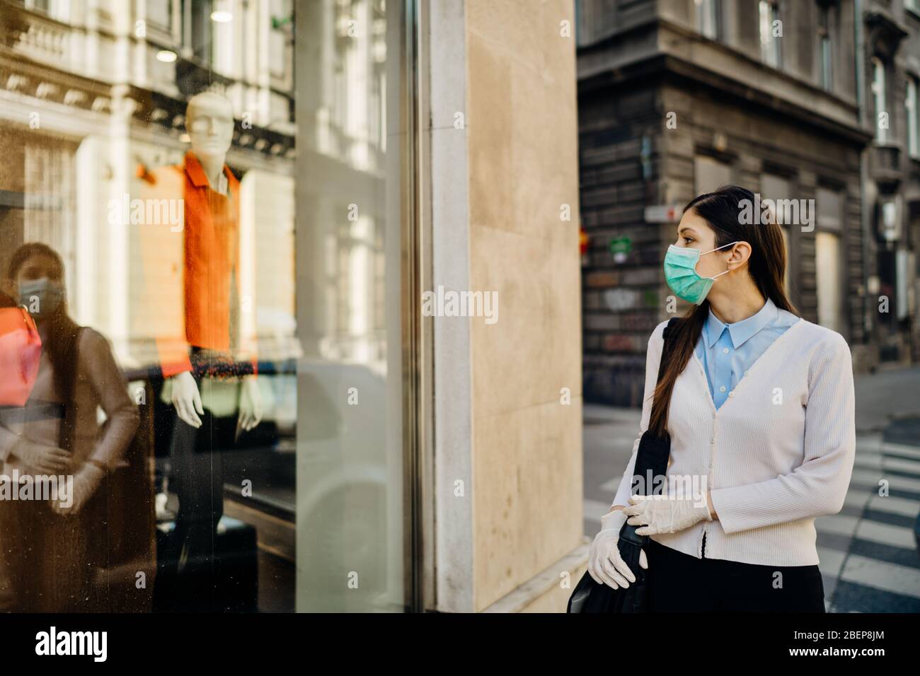 Donna con maschera che guarda un chiuso di moda vestiti storefront.Abbigliamento shopping durante lo spegnimento focolaio di coronavirus.COVID-19 abbigliamento di quarantena Foto Stock