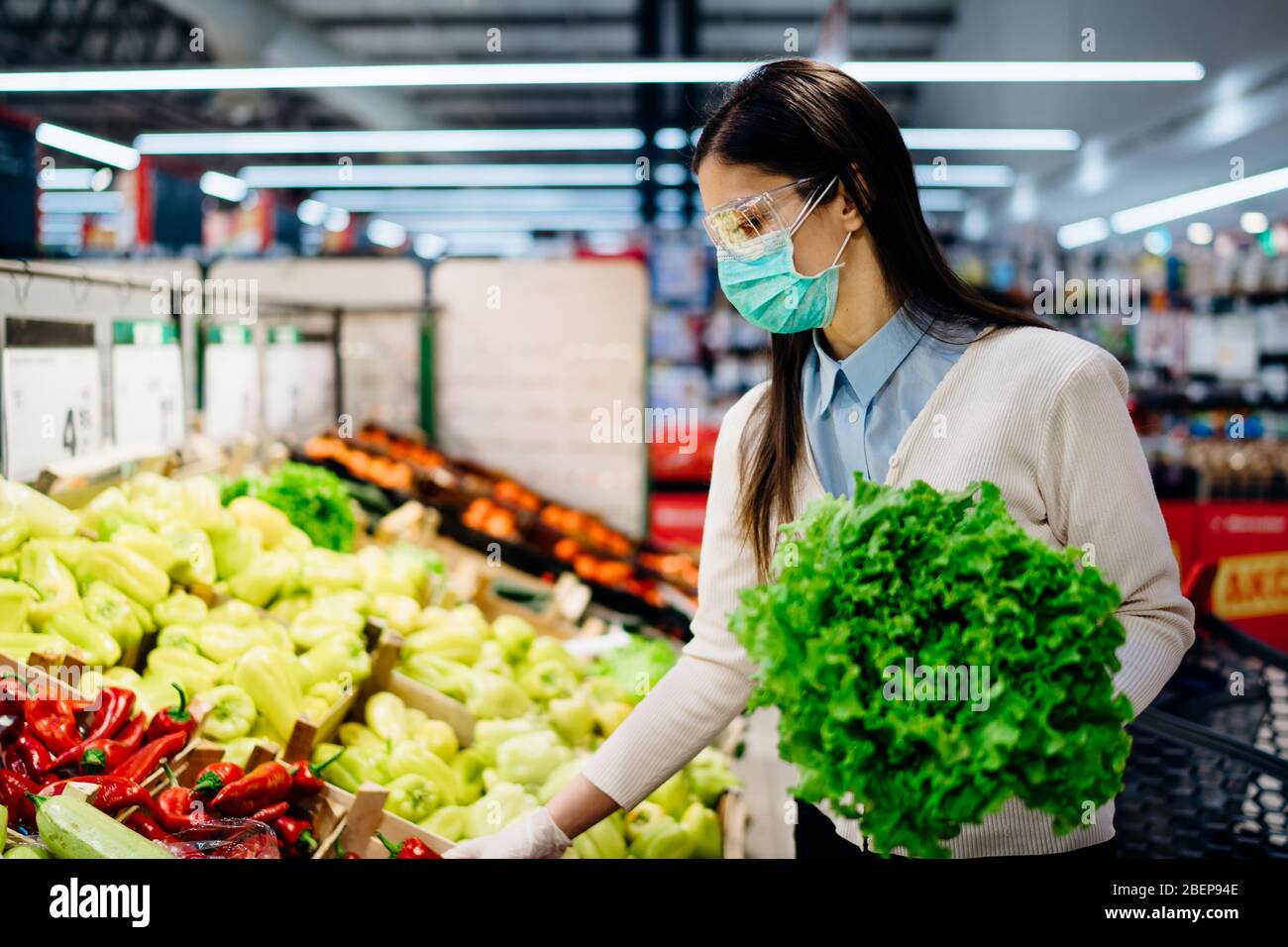 Donna con maschera igienica acquisto in supermercato negozio di alimentari per i verdi freschi, bilancio di shopping durante la pandemic.Natural fonte di vitamine e minatore Foto Stock