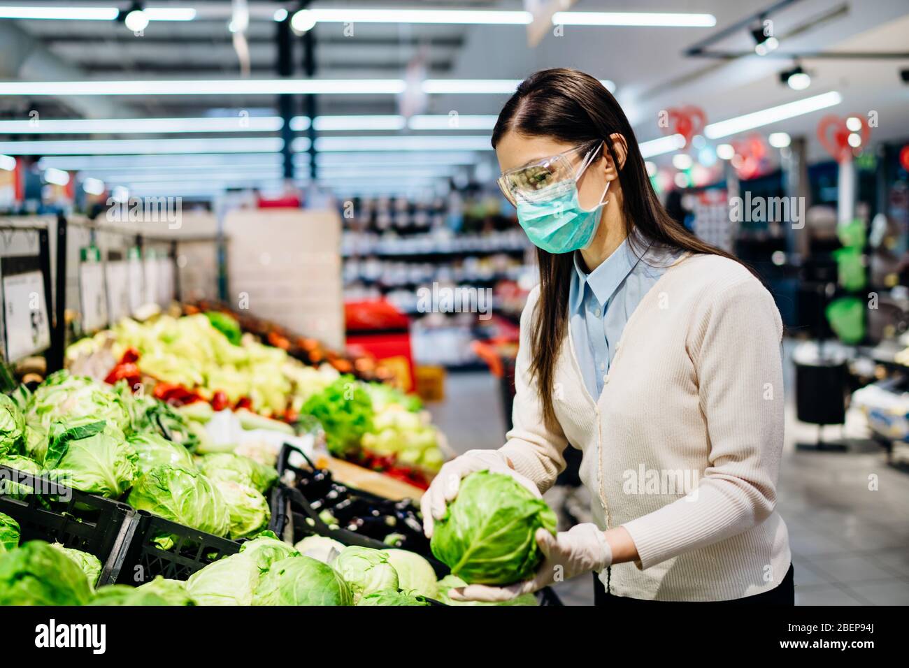 Donna con maschera igienica acquisto in supermercato negozio di alimentari per verdi freschi, bilancio di shopping per le forniture durante il pandemic.Buying biologico vegetabl Foto Stock