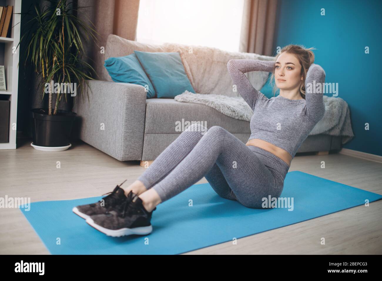 Giovane donna attiva in abbigliamento sportivo facendo esercizi di fitness per abs mentre si sdraiato su tappetino yoga a casa. Concetto di autodisciplina e motivazione. Foto Stock