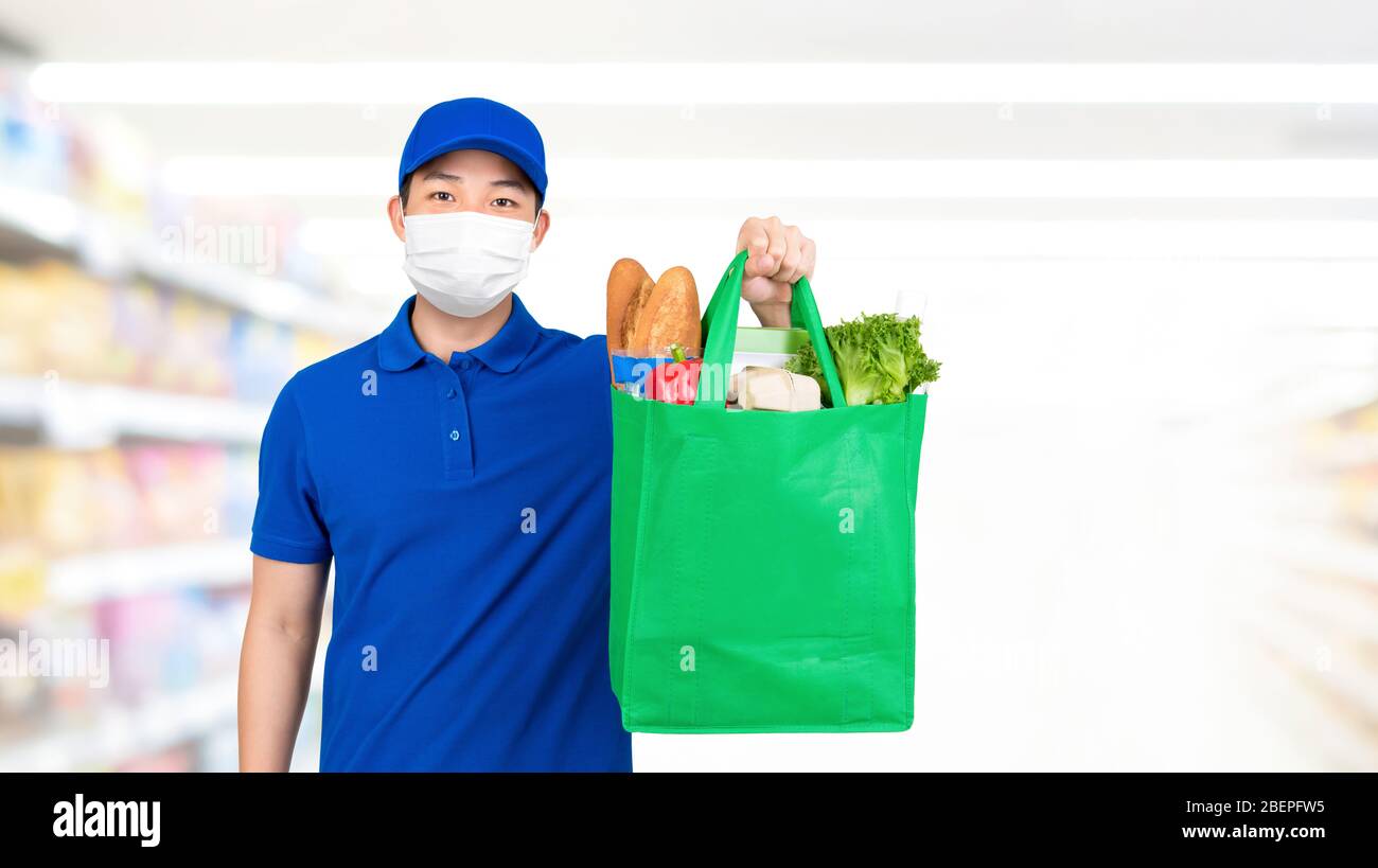 Uomo igienico che indossa la maschera medica che tiene la borsa della spesa della drogheria nel supermercato che offre il servizio di consegna domestico Foto Stock