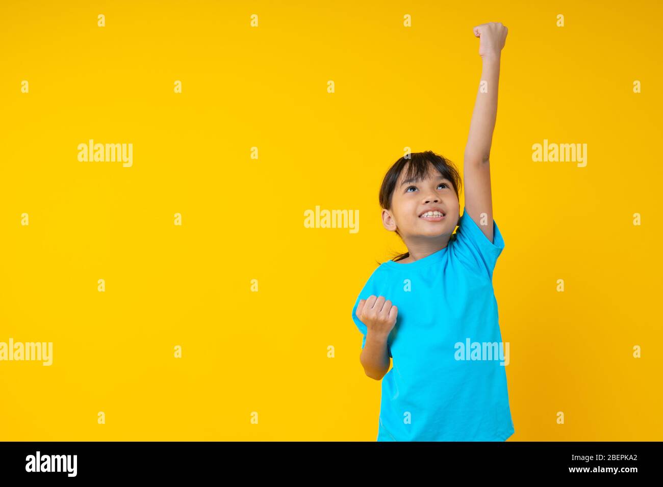Allegro sorridente bambina tailandese mostra mano fino a volare, bambino asiatico contro muro giallo in studio Foto Stock