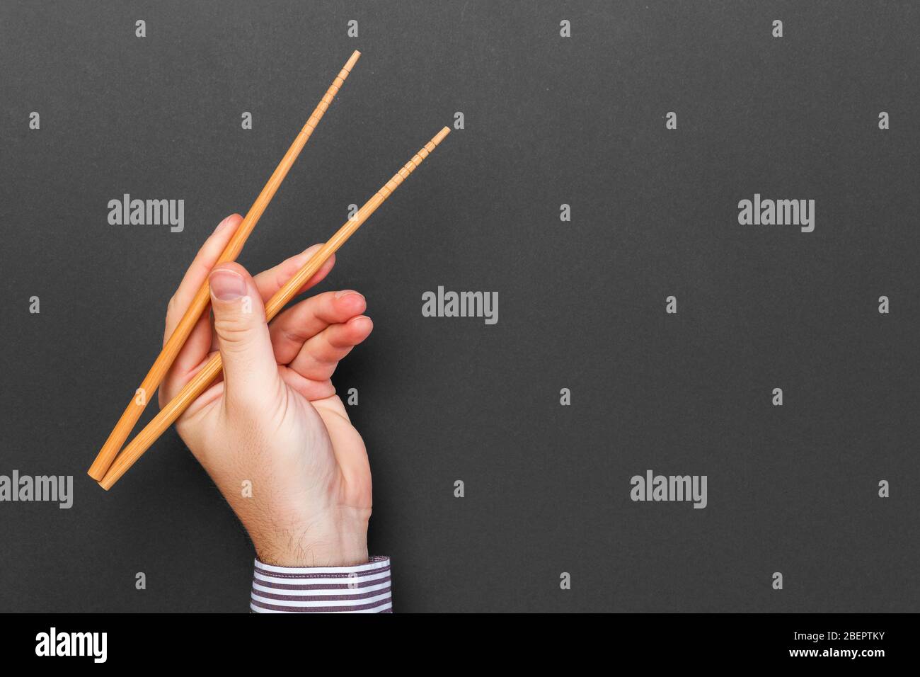 Immagine creativa delle bacchette di legno nelle mani di sesso maschile su sfondo nero. Il giapponese e il cinese del cibo con copia spazio. Foto Stock