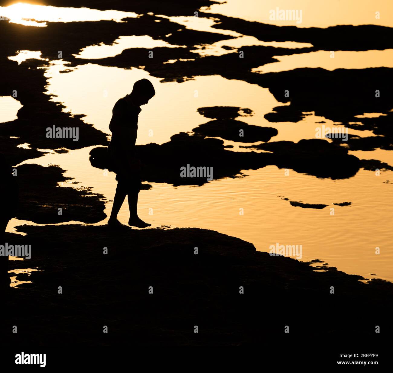 Silhouette di un bambino che esplora le piscine di roccia al tramonto, Akko, Israele Foto Stock