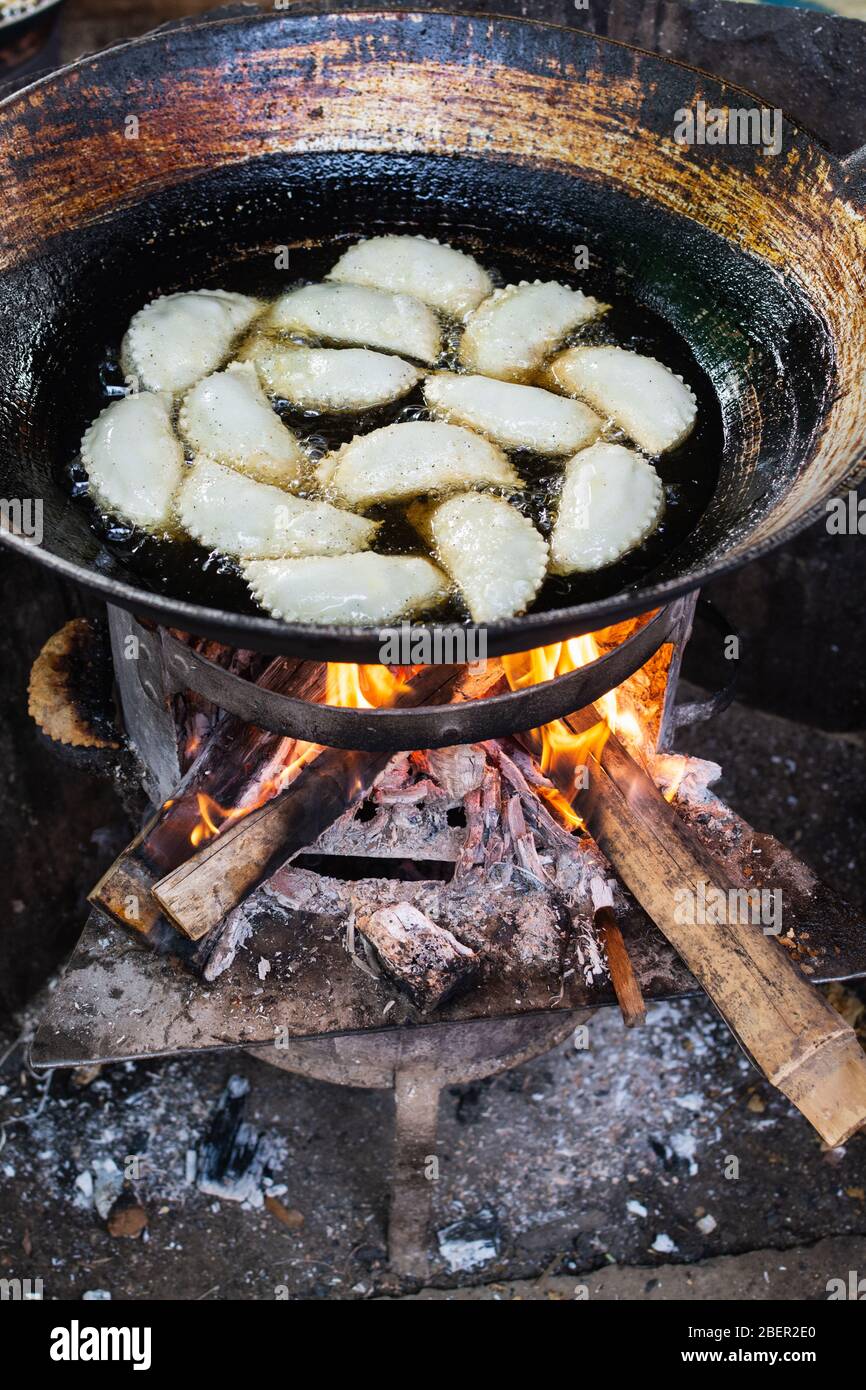 Gnocchi di pasta friggendo in olio su stufa a legna. Bancarelle alimentari asiatiche nel mercato di Indein, Myanmar. Orientamento verticale Foto Stock