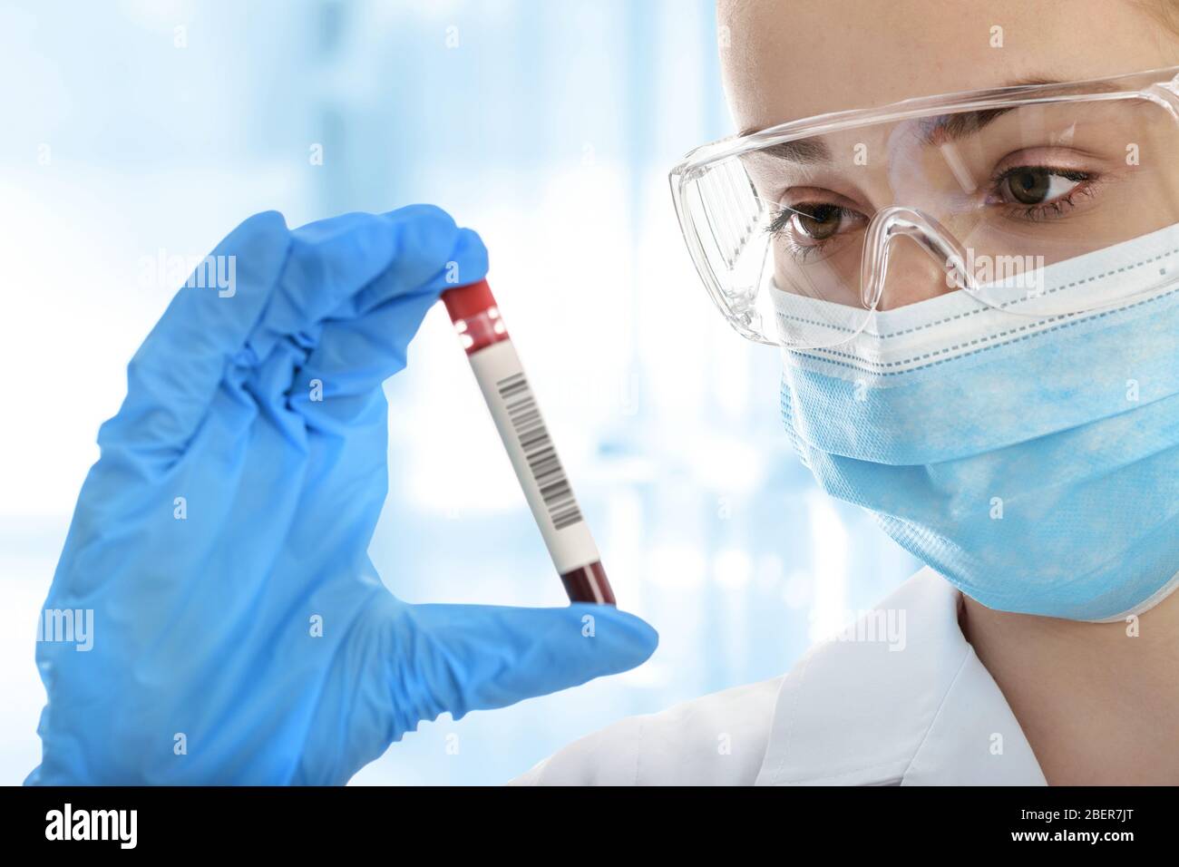 Giovane donna in un laboratorio medico per l'analisi di indumenti protettivi della provetta per il campione di sangue Foto Stock