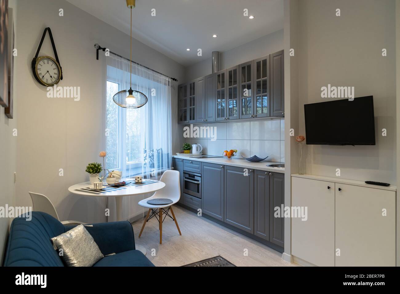 Elegante e accogliente design interno cucina nel moderno monolocale. Mobili da cucina vicino alla finestra e zona riposo con divano e TV Foto Stock