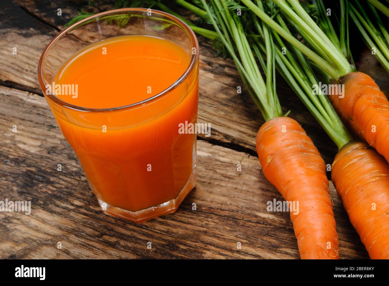 Bicchiere di succo di carota fresco e mazzo di carote organiche crude su un tavolo rustico in legno Foto Stock