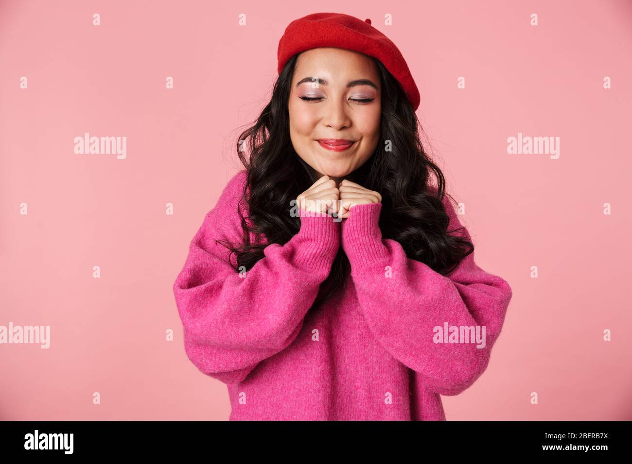 Immagine di giovane bella ragazza asiatica che indossa beret sorridente e clenching le sue pugni al petto isolato su sfondo rosa Foto Stock