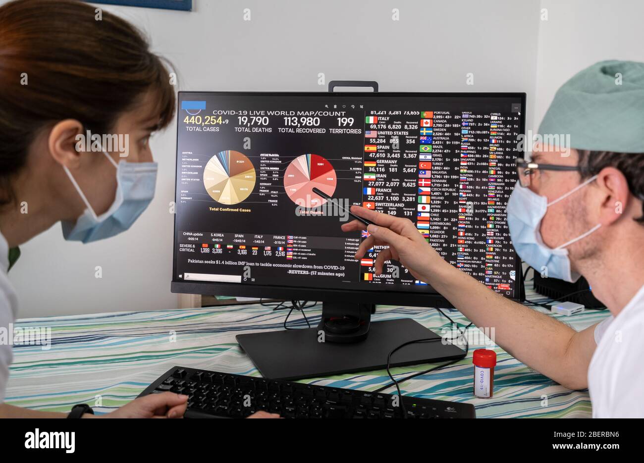 Medici e infermieri che guardano i dati e la grafica dei casi di Coronavirus, colpiti e morti nel mondo su uno schermo di computer. Foto Stock