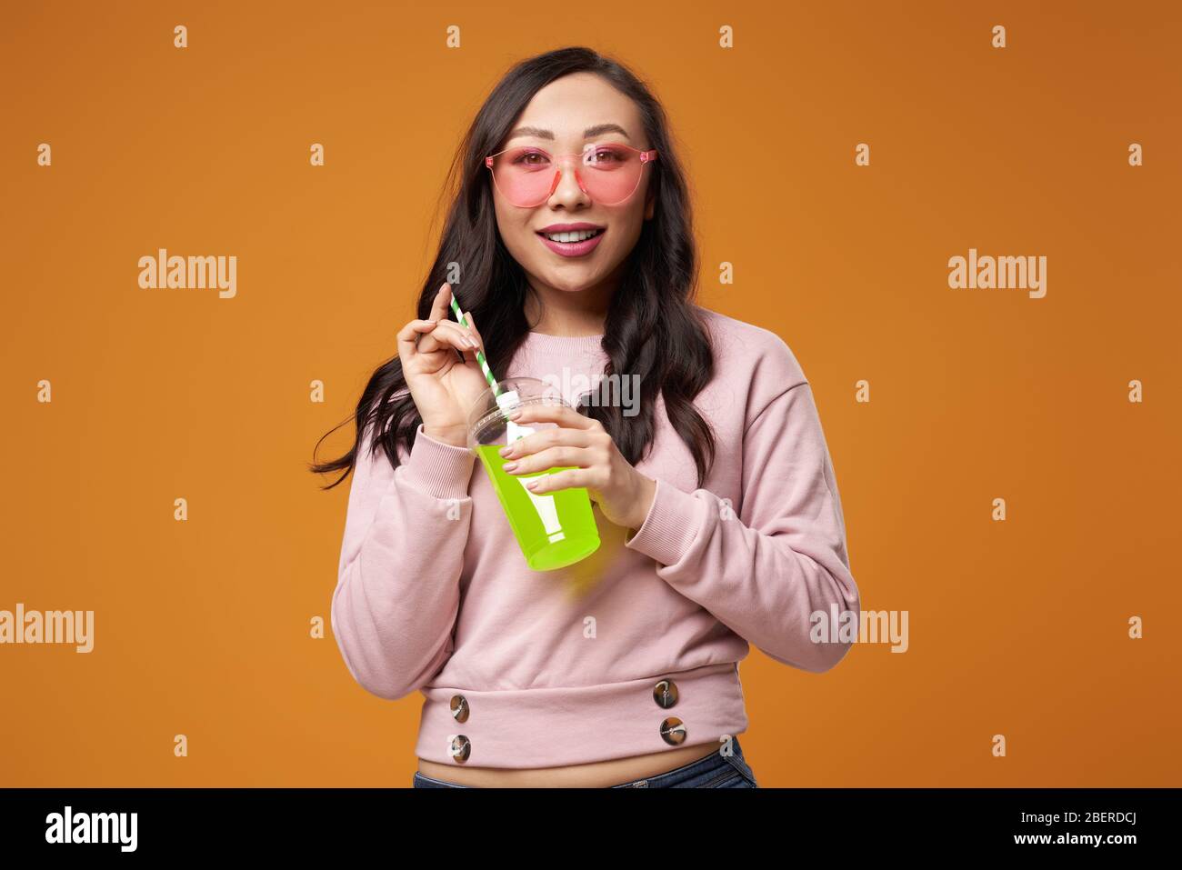Donna bruna felice in bicchieri rosa con cocktail su sfondo giallo vuoto in studio Foto Stock