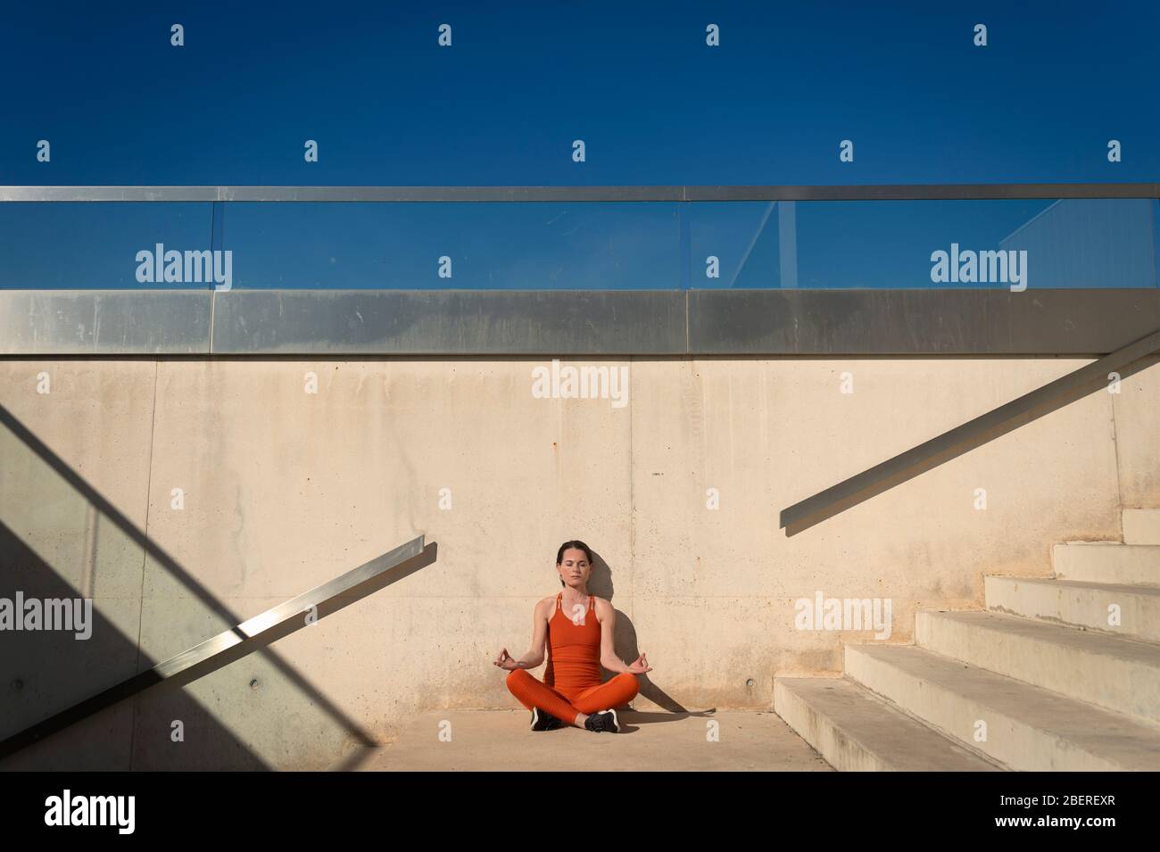 donna che pratica yoga e medita al sole, ambiente urbano con passi concreti Foto Stock