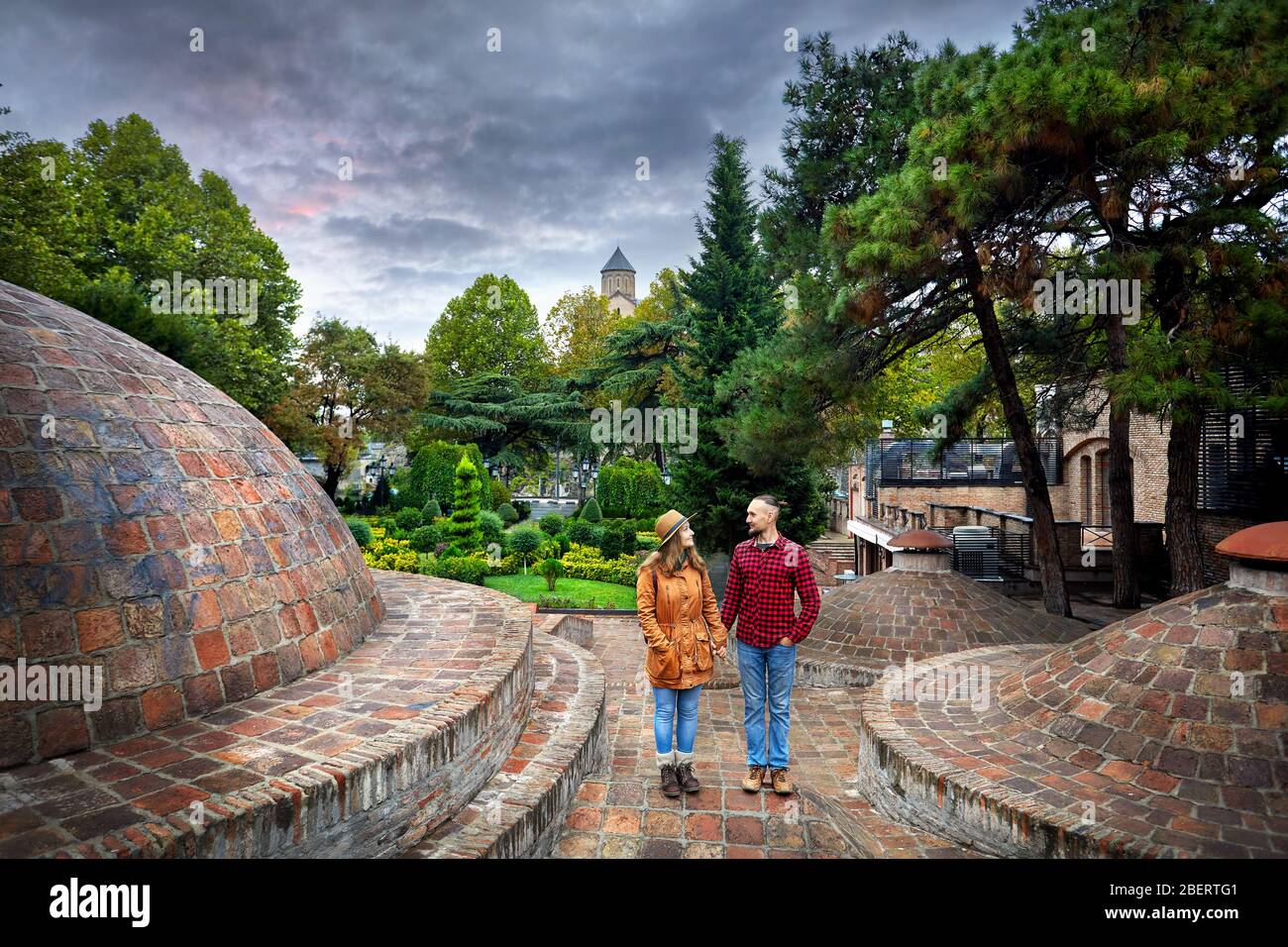 Tourist donna in giacca marrone e Uomo in camicia rossa in piedi vicino alla cupola di pubblico bagno solforico quartiere centrale di Tbilisi, Georgia Foto Stock