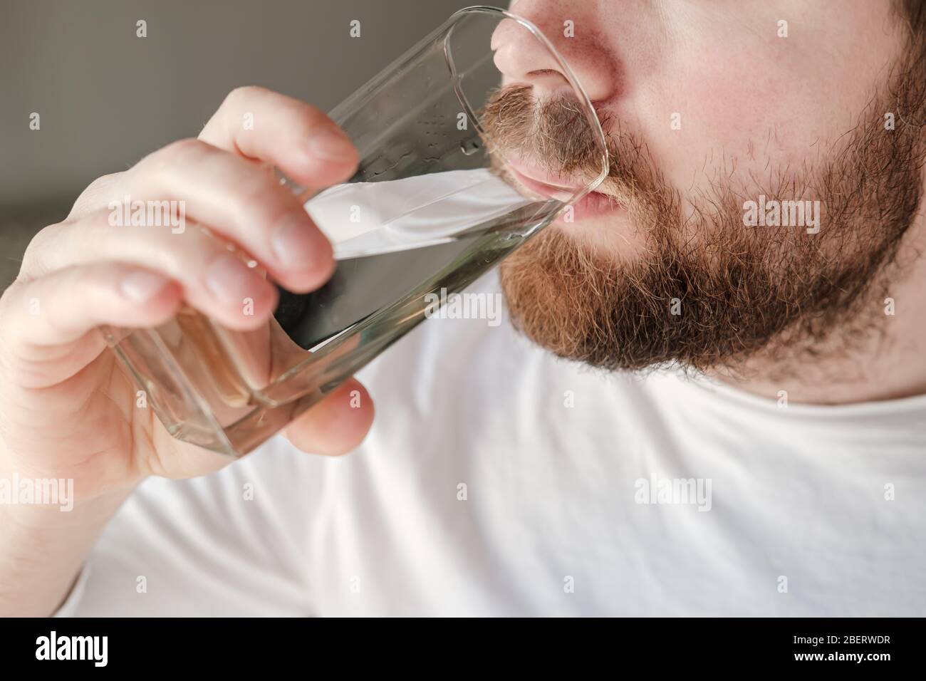 Primo piano di un uomo barbuto che beve acqua fresca e pulita da un bicchiere. Concetto di salute. Foto Stock Primo piano di un uomo barbuto che beve acqua fresca e pulita da un bicchiere. Concetto di salute. Foto Stock